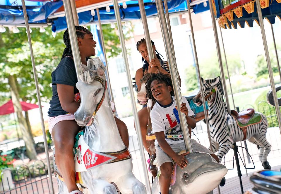 Jurnee Darks, 10, left, laughs with K'dyn Smith, 8, center, and Cynical Williamson, 10, back, while riding the carousel at Columbus Commons on July 20.