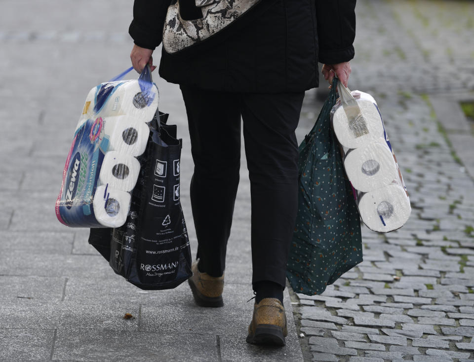 A woman carries her shopping including bags of toilet paper, in downtown Frankfurt, Germany, Wednesday, March 18, 2020. Because of the spread of the coronavirus, bars, cinemas, theatres, museums, and many shops are now closed. For most people, the new coronavirus causes only mild or moderate symptoms. For some it can cause more severe illness. (Arne Dedert/dpa via AP)