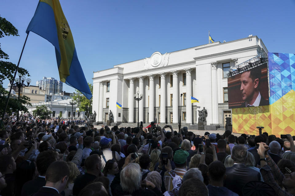 People gather in front of Verkhovna Rada, the Ukrainian parliament, during the inauguration ceremony of new Ukrainian President Volodymyr Zelenskiy, right on the screen, in Kiev, Ukraine, Monday, May 20, 2019. Television star Volodymyr Zelenskiy has been sworn in as Ukraine's next president after he beat the incumbent at the polls last month. The ceremony was held at Ukrainian parliament in Kiev on Monday morning. (AP Photo/Evgeniy Maloletka)