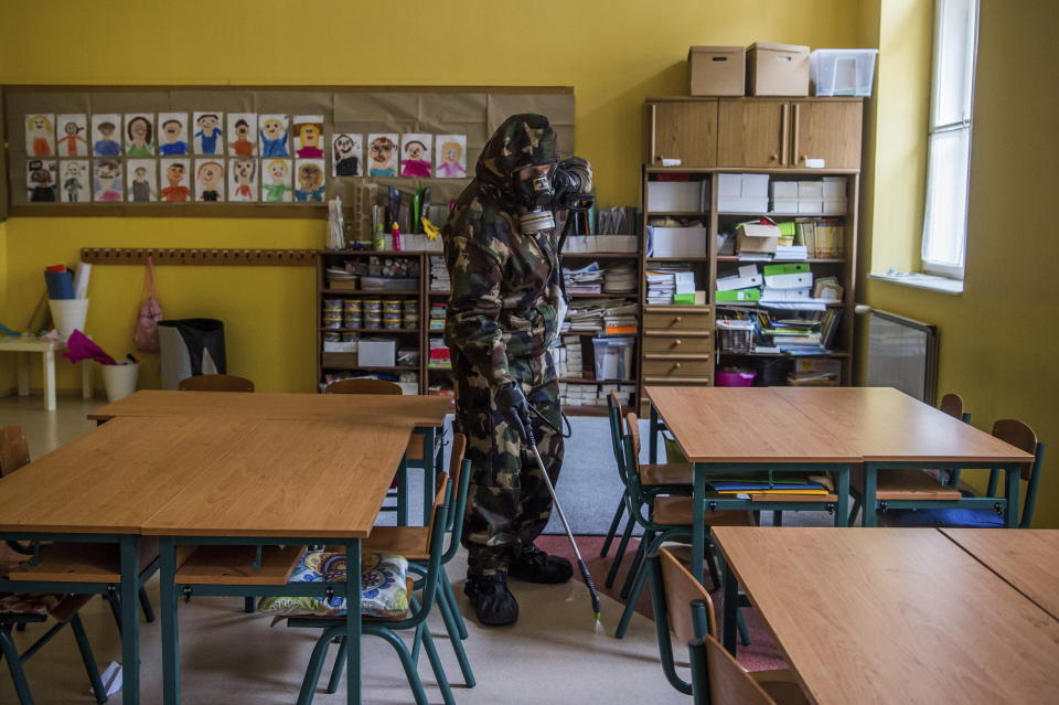 A Hungarian soldier wearing a hazmat suit disinfects a classroom of a combined kindergarten and elementary school in an effort to curb the spread of the pandemic of the new coronavirus in Budapest, Hungary, Wednesday, March 17, 2021. (Zoltan Balogh/MTI via AP)