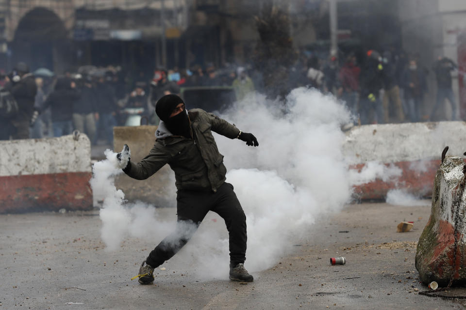 A protester throw back a tear gas canisters towards riot policemen, during a protest against deteriorating living conditions and strict coronavirus lockdown measures, in Tripoli, north Lebanon, Thursday, Jan. 28, 2021. Violent confrontations overnight between protesters and security forces in northern Lebanon left a 30-year-old man dead and more than 220 people injured, the state news agency said Thursday. (AP Photo/Hussein Malla)