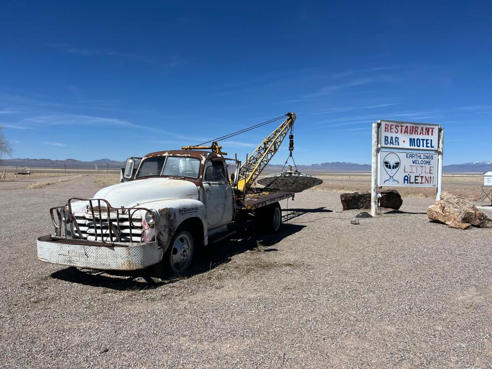 An old tow truck carrying a flying saucer, and a sign that reads "Restaurant, bar, motel: earthlings welcome Little A'le'inn."