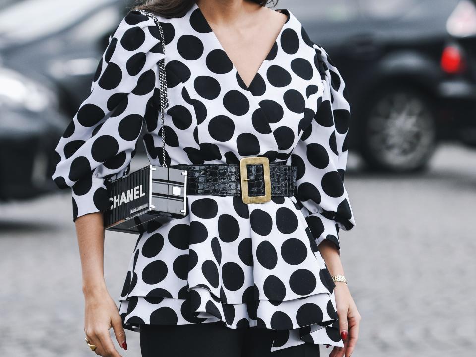 woman on the street wearing a structured boxy black and white polka dot top over black trousers