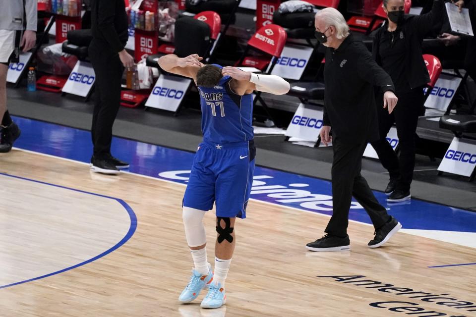 Dallas Mavericks guard Luka Doncic (77) pulls his jersey over his face after attempting a final-second shot that he did not make as San Antonio Spurs head coach Gregg Popovich, right rear, looks on during an NBA basketball game in Dallas, Sunday, April 11, 2021. (AP Photo/Tony Gutierrez)