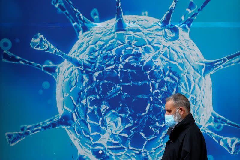 FOTO DE ARCHIVO. Un hombre con una mascarilla pasa por delante de una ilustración de un virus fuera de un centro científico regional, en Oldham, Gran Bretaña.