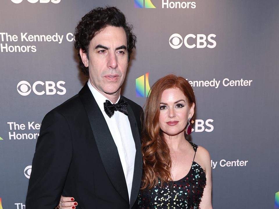 sacha baron cohen and isla fisher on a red carpet for the kennedy center honors, wearing black formal clothing and posing together