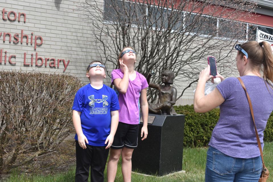 Jessie Schilz of Clinton, right, takes a photograph of her children, Ali and Will Schilz as they watch the progression of Monday's April 8, 2024, solar eclipse during a public eclipse viewing party at the Clinton Township Public Library.