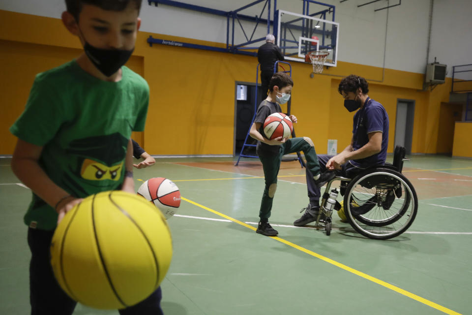 Adolfo Damian Berdun, of Argentina, a professional player and captain of the Argentine basketball Paralympic team, teaches children basketball at a primary school in Verano Brianza, outskirt of Milan, Italy, Tuesday, May 11, 2021. Four second-grade classes in the Milan suburb of Verano Brianza have been learning to play basketball this spring from a real pro. They also getting a lesson in diversity. Their basketball coach for the last month has been Adolfo Damian Berdun, an Argentinian-Italian wheelchair basketball champion. Berdun, 39, lost his left leg in a traffic accident at ag 13 in his native Buenos Aires, and he has visited many schools over the years to discuss how he has lived with his disability. (AP Photo/Luca Bruno)