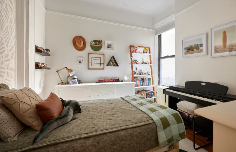 Organ at end of twin bed in neutral bedroom with dresser and ladder bookshelf.