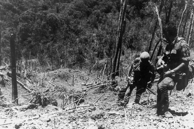 A U.S. Army photographer and assistant climb through the devastated landscape on Dong Ap Bia in South Vietnam on May 31, 1969, 11 days after U.S. forces captured the island in the so-called battle of Hamburger Hill during the Vietnam War. File Photo courtesy of the U.S. Army Military History Institute