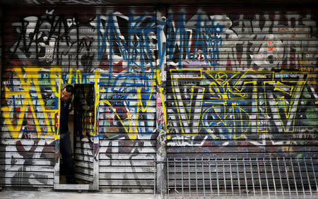 A man looks out of a door of his shop tagged by "pichadores", graffiti artists who tag buildings and landmarks with angular, runic fonts, with their personal signatures, called "pichacao", on a street in Sao Paulo, Brazil, April 20, 2017. REUTERS/Nacho Doce