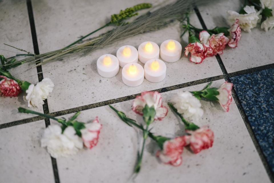 Flowers and faux candles on a tiled floor are part of a memorial