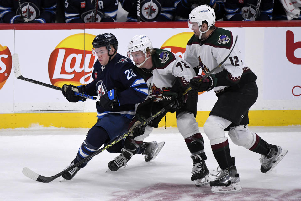 Winnipeg Jets center Karson Kuhlman (20) is checked by Arizona Coyotes center Travis Boyd (72) and Coyotes left wing Nick Ritchie (12) during the first period of an NHL hockey game in Winnipeg, Manitoba, on Sunday Jan. 15, 2023. (Fred Greenslade/The Canadian Press via AP)