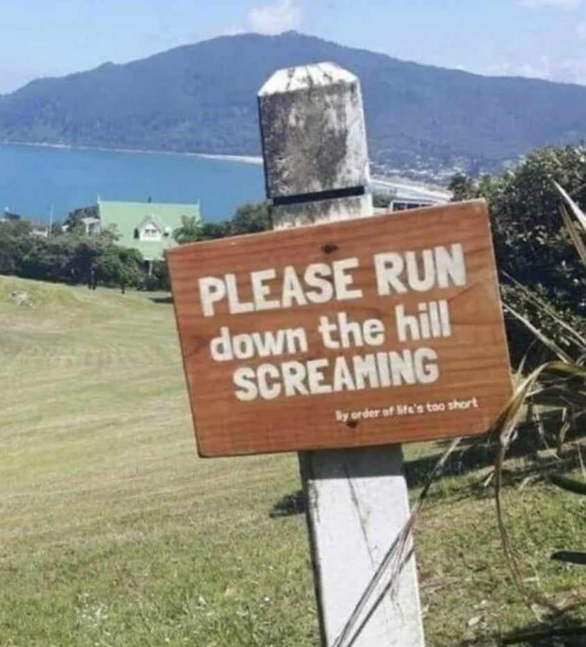 Sign reads "PLEASE RUN down the hill SCREAMING" with "By order of life's too short" below, near a hill