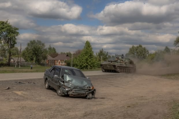 A Ukrainian self-propelled howitzer is seen driving past a damaged car, in Vovchansk on Sunday.