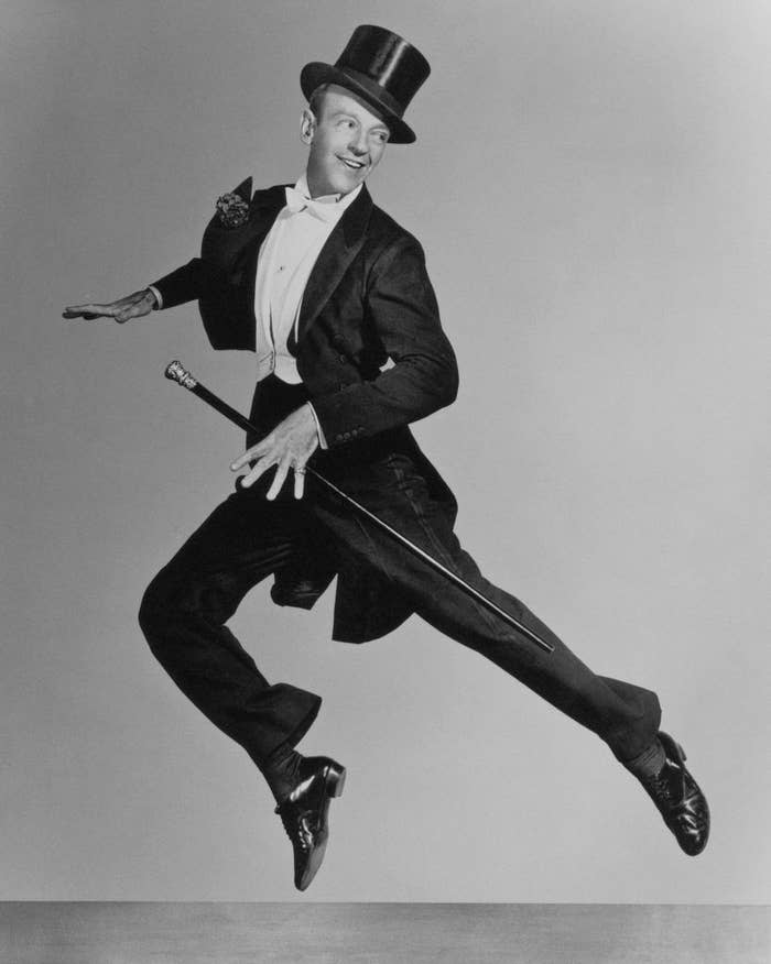 Fred Astaire, wearing a tuxedo with tails and a top hat, performs a mid-air dance pose while holding a cane