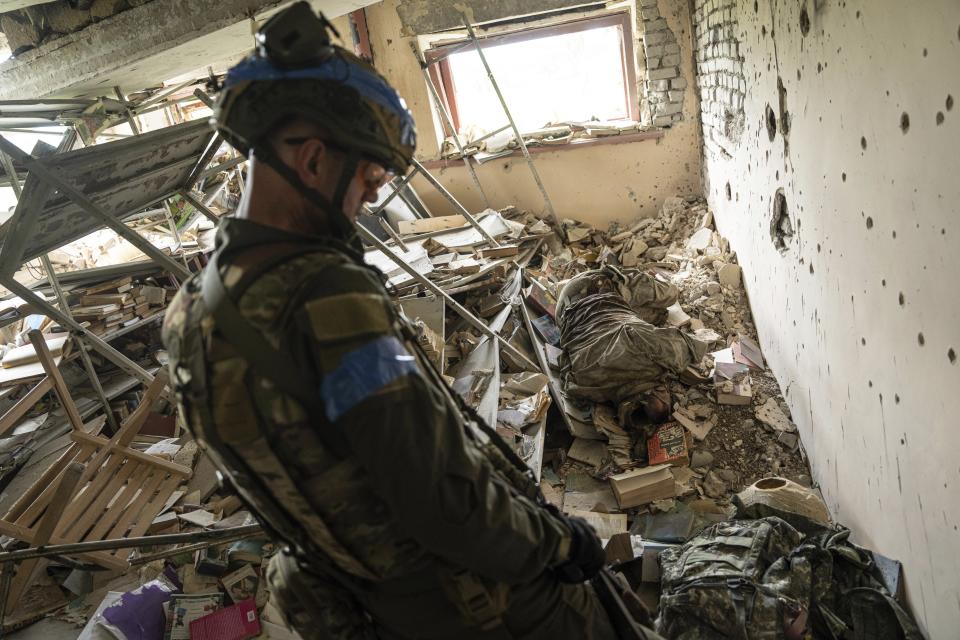 A Ukrainian commander, aka Lermontov, of the 68th Oleksa Dovbush hunting brigade, walks past the body of a killed Russian soldier in the recently retaken village of Blahodatne, Ukraine, Saturday, June 17, 2023. (AP Photo/Evgeniy Maloletka)