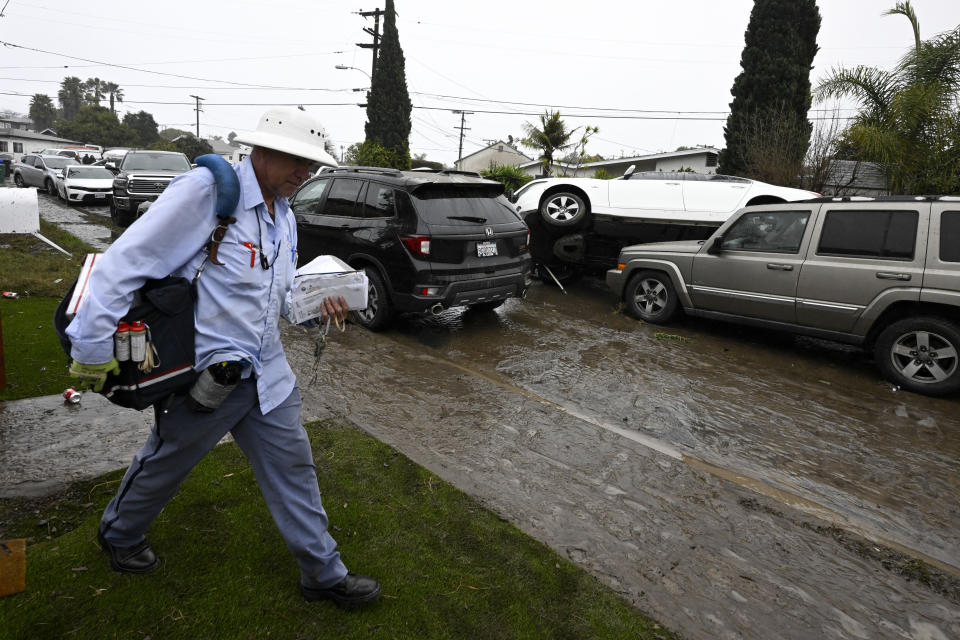 Mail carrier Felipe Estrada delivers mail in front of cars moved by flooding during a rainstorm Monday, Jan. 22, 2024, in San Diego. (AP Photo/Denis Poroy)