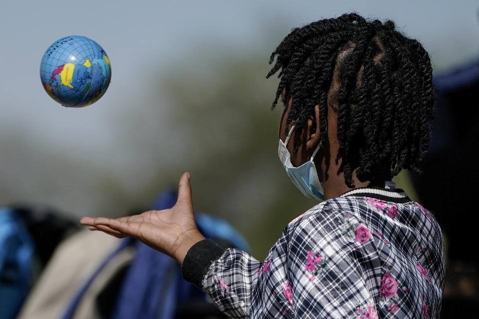 A Haitian migrant girl plays with a ball in the shape of a globe while waiting to board a bus to Houston provided by a humanitarian group after she and her family were released from U.S. Customs and Border Protection custody, Friday, Sept. 24, 2021, in Del Rio, Texas. (AP Photo/Julio Cortez)