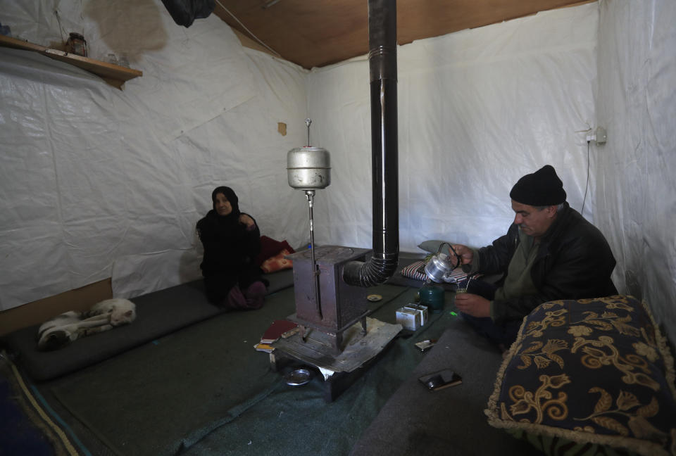 A Syrian displaced man Mohammed Zakaria, 53, who fled his Syrian hometown of Homs in 2012, prepares a hot drink as he sits inside his tent with his wife, left, at a refugee camp, in Bar Elias, in eastern Lebanon's Bekaa valley, Friday, March 5, 2021. Nearly ten years later, the family still hasn't gone back and Zakaria is among millions of Syrians unlikely to return in the foreseeable future, even as they face deteriorating living conditions abroad. The Syrian conflict has resulted in the largest displacement crisis since World War II. (AP Photo/Hussein Malla)