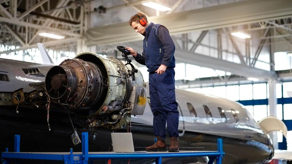 Aircraft engineer in the hangar repairing and maintaining airplane jet engine.