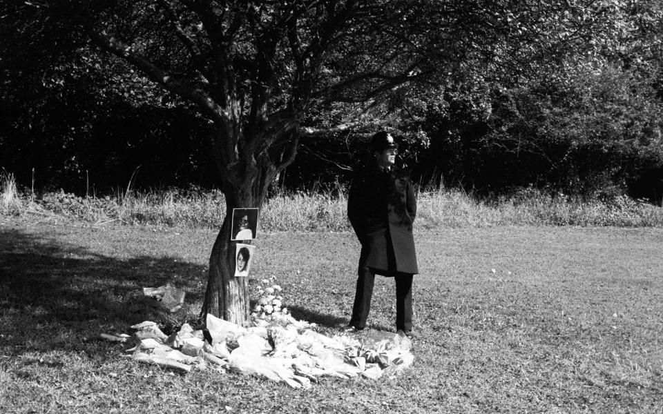 A policeman stands guard next to a tree surrounded by floral tributes in Wild Park, Brighton where the bodies of Nicola and Karen were found in 1986