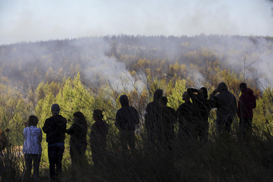 Local residents look at a fire burning just outside their village of Charneca, in the Sintra national park, west of Lisbon, Sunday, Oct. 7, 2018. Over 700 firefighters were battling a forest fire that started overnight about 40 kilometers (25 miles) west of Lisbon. (AP Photo/Armando Franca)