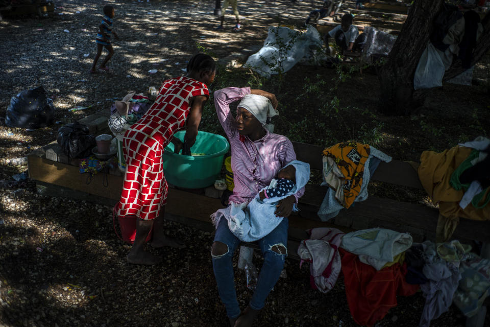 A woman washes clothes next to a woman cradling her baby at the Hugo Chavez public square transformed into a refuge for families forced to leave their homes due to clashes between armed gangs in Port-au-Prince, Haiti, Thursday, Oct. 20, 2022. (AP Photo/Ramon Espinosa)