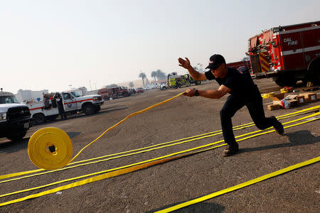 A Cal Fire firefighter unrolls new hoses before they are packed to fight wildfire at the Ventura County Fairgrounds fire camp during the Thomas fire in Ventura, California, U.S. December 12, 2017. REUTERS/Patrick T Fallon