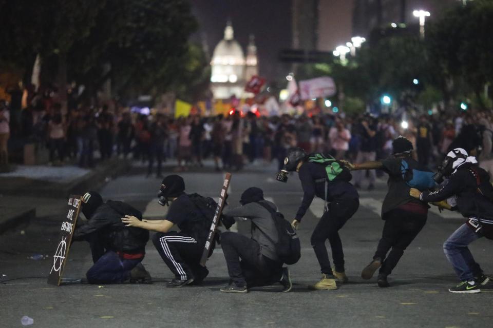 Gas mask wearing demonstrators take cover as they face off with police as they protest government proposed changes to work rules and pensions in Rio de Janeiro, Brazil, Wednesday, March 15, 2017. Critics say the changes would reduce job security for Brazilian workers and the pension proposal would force many people to work longer to qualify for pensions and reduce retirement benefits for many. (AP Photo/Leo Correa)