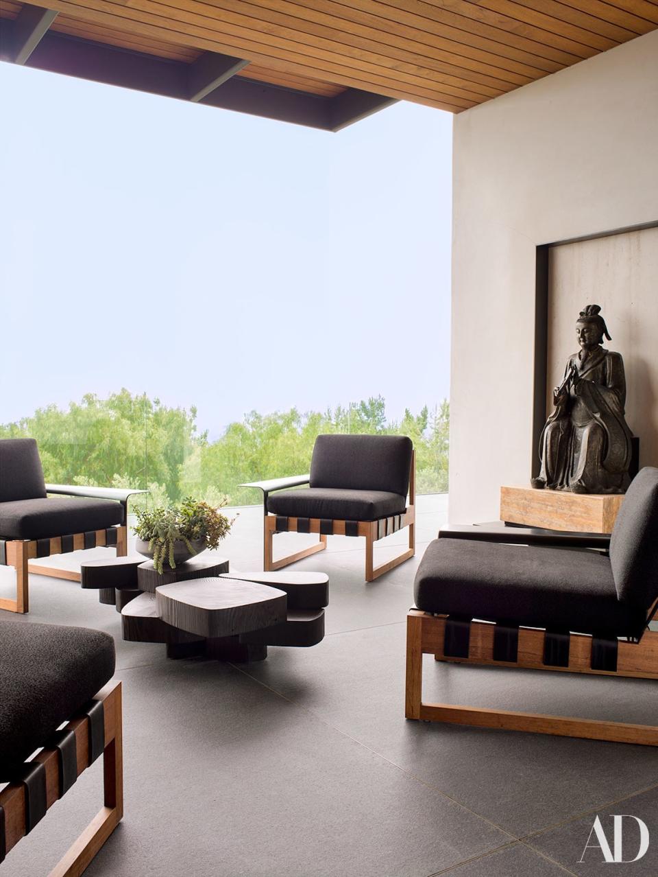 Custom teak, leather, and bronze chairs by Shadley surround a cocktail table on a terrace. Antique bronze Chinese statue.