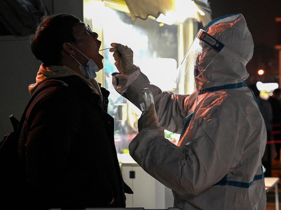 A health worker in Personal Protective Equipment (PPE) suit takes a swab sample from a man to test for the Covid-19 coronavirus in Beijing on January 18, 2022.