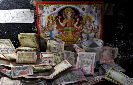 500 and 1000 Indian rupee banknotes are kept in front of an image of the Hindu deities at a cash counter inside a bank in Jammu, November 10, 2016 REUTERS/ Mukesh Gupta