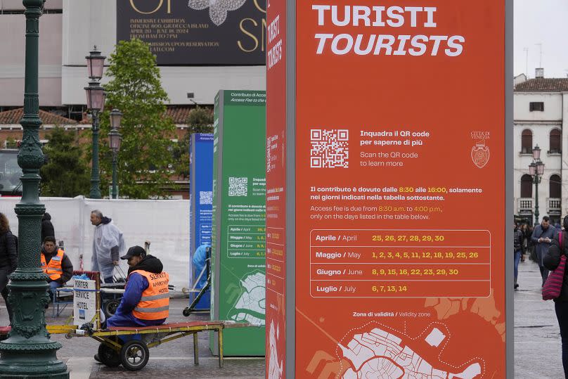 A porter waits for tourists outside the main train station in Venice next to totem's explanation for tourist entrance tax