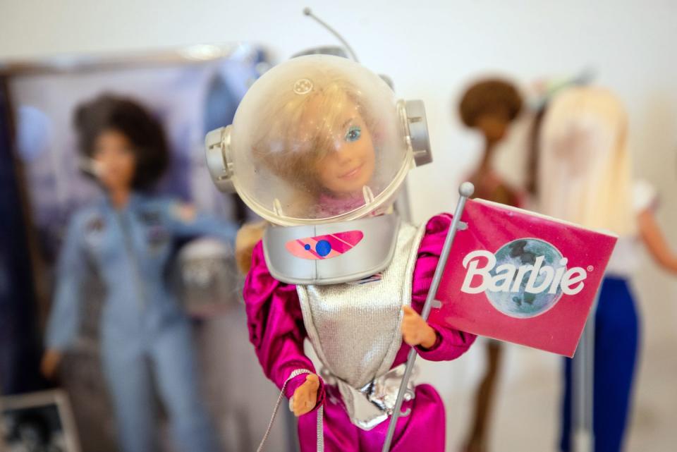 barbie wearing a pink and silver astronaut suit and helmet, holding a pink barbie flag