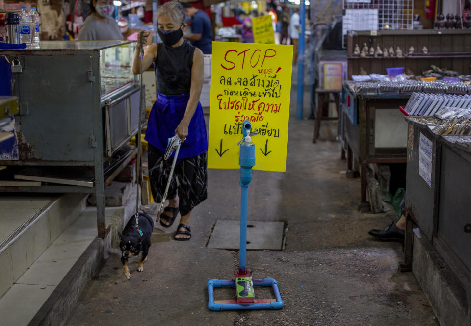 A woman walks her dog past a hand sanitizer positioned in an amulet market in Bangkok, Thailand, Tuesday, June 2, 2020. Amulet markets were allowed to reopen on Monday, June 1, 2020 as the Thai government continues to ease restrictions related to running business in the capital Bangkok that were imposed weeks ago to combat the spread of COVID-19. Believers in amulets say they can bring good fortune, true love or just about anything else. Sign reads as "Stop. Use hand gel before walking in. Please cooperate. Step beneath to pump" (AP Photo/Gemunu Amarasinghe)