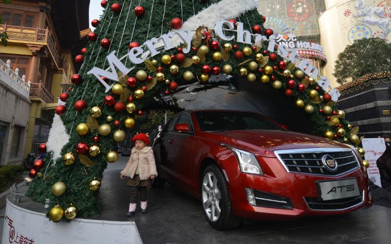A child stands next to a Christmas tree commercial for a car brand outside a shopping centre in Shanghai on December 24, 2013