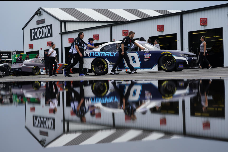 Crew members are reflected in a puddle as they push the car of Landon Cassill through the garage area during inspections for Saturday's NASCAR Xfinity Series auto race at Pocono Raceway, Friday, July 22, 2022, in Long Pond, Pa. (AP Photo/Matt Slocum)