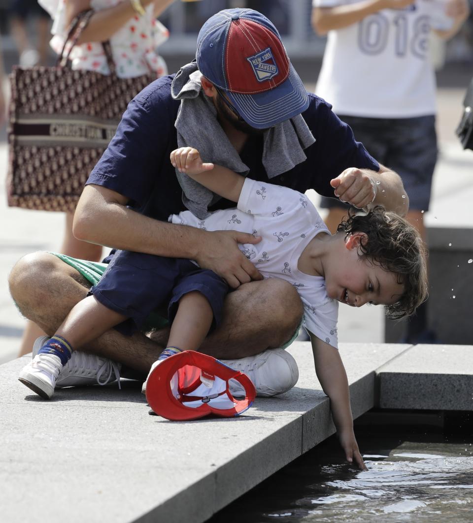 Joseph Setton and his son, Sion Setton, cool off with water from a fountain during the second round of the U.S. Open tennis tournament, Wednesday, Aug. 29, 2018, in New York. (AP Photo/Seth Wenig)