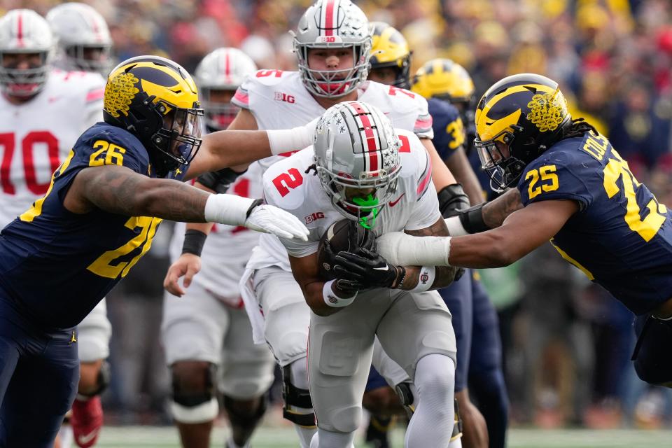 Michigan defensive lineman Rayshaun Benny (26) and linebacker Junior Colson (25) tackle Ohio State receiver Emeka Egbuka.