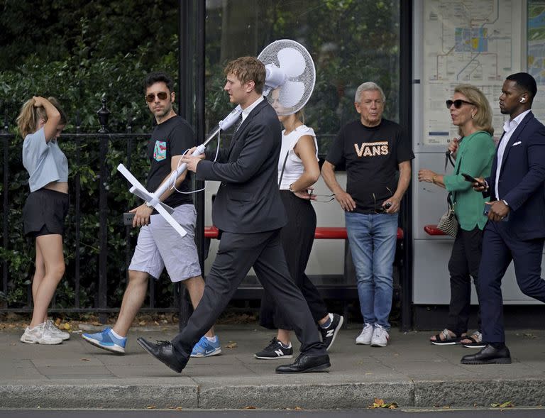 Um funcionário de escritório carrega um ventilador por Westminster, no centro de Londres, na terça-feira, 12 de julho de 2022. O Met Office emitiu um alerta meteorológico âmbar para calor extremo em partes do Reino Unido antes que as temperaturas subam esta semana.  (Yui Mok/PA via AP)