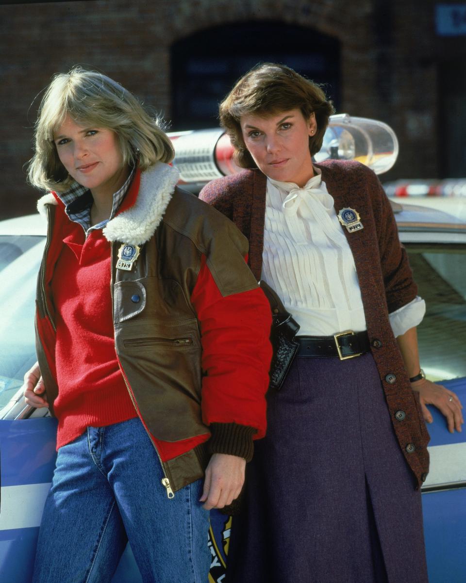 Actors Sharon Gless (L) and Tyne Daly, both wearing police badges, lean against a police car in a promotional portrait for the television series, 'Cagney & Lacey,' c. 1982.