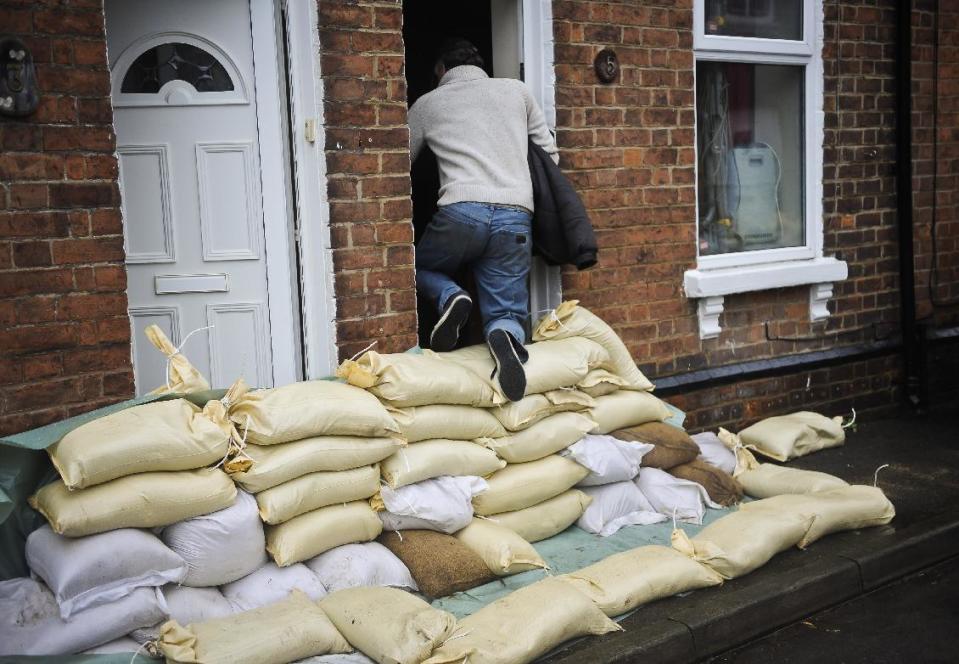 A local resident climbs over a sandbag levee protecting the front doors of homes in Gloucester, southwest England, as the region reacts to an increased flood threat alert Friday Feb. 14, 2014. Many regions of Britain have been warned to expect severe weather over the coming days from heavy rainfall, gale-force winds and snow.(AP Photo/Ben Birchall, PA) UNITED KINGDOM OUT - NO SALES - NO ARCHIVES