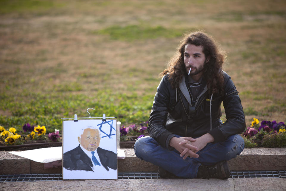 An Israeli man sits next to a painting of former Israeli Prime Minister Ariel Sharon next to his coffin at the Knesset plaza, in Jerusalem, Sunday, Jan. 12, 2014. Sharon, the hard-charging Israeli general and prime minister who was admired and hated for his battlefield exploits and ambitions to reshape the Middle East, died Saturday, eight years after a stroke left him in a coma from which he never awoke. He was 85. (AP Photo/Oded Balilty)