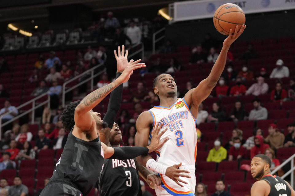 Oklahoma City Thunder guard Shai Gilgeous-Alexander (2) drives to the basket as Houston Rockets center Christian Wood, left, and Kevin Porter Jr. (3) defend during the first half of an NBA basketball game, Monday, Nov. 29, 2021, in Houston. (AP Photo/Eric Christian Smith)
