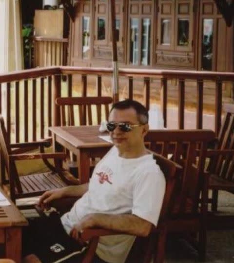 A man with sunglasses sits on outdoor furniture. 