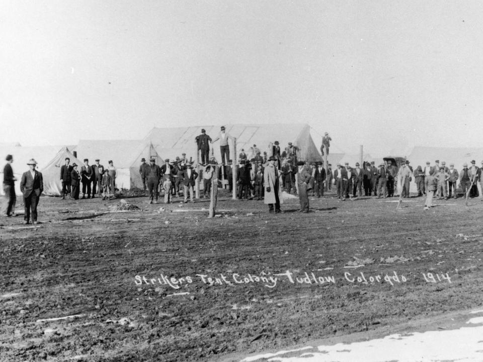 people standing around an open field in ludlow, colorado, with tents in the background