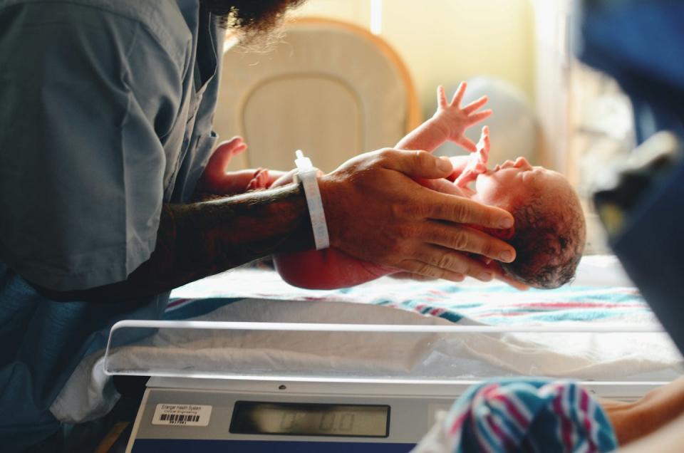 Close-up of person holding premature baby above a scale