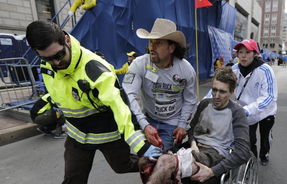 FILE - In this April 15, 2013 file photo, an emergency responder and volunteers, including Carlos Arredondo, center, in the cowboy hat, push Jeff Bauman in a wheel chair after he was injured in an explosion near the finish line of the Boston Marathon, in Boston. On Saturday, May 10, 2014, Arredondo and Bauman both received honorary degrees and gave graduation speeches during commencement ceremonies for Fisher College in Boston. (AP Photo/Charles Krupa, File)