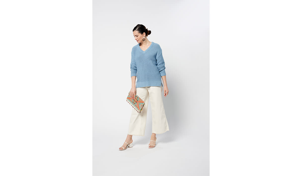 Woman wearing light blue v-neck sweater with wide leg white pants and heels